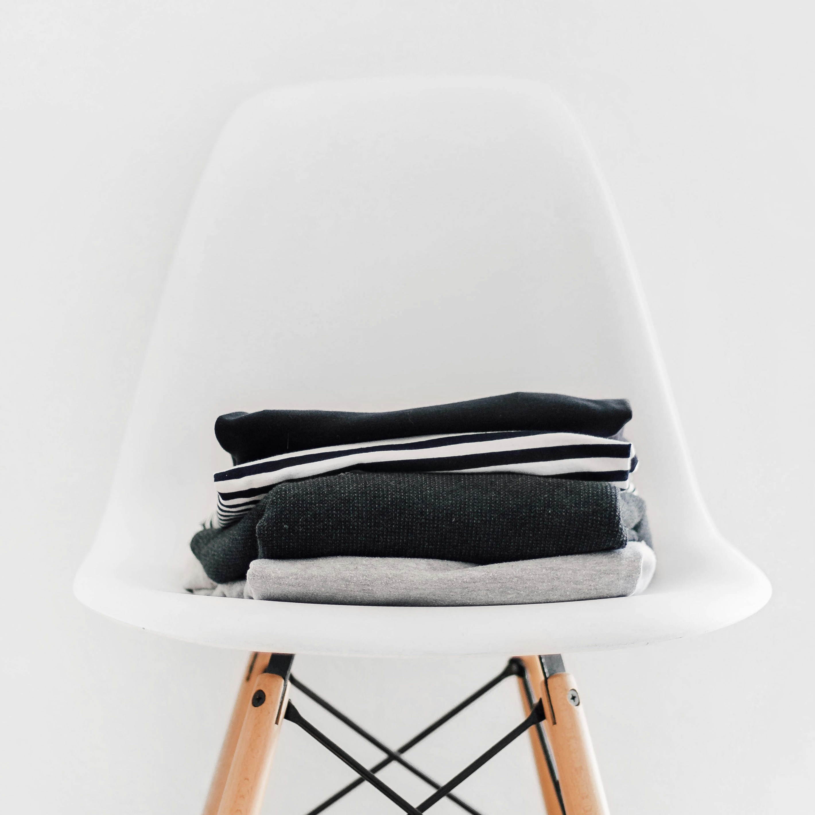 pile of black, white, and gray textiles on white padded chair with brown frame