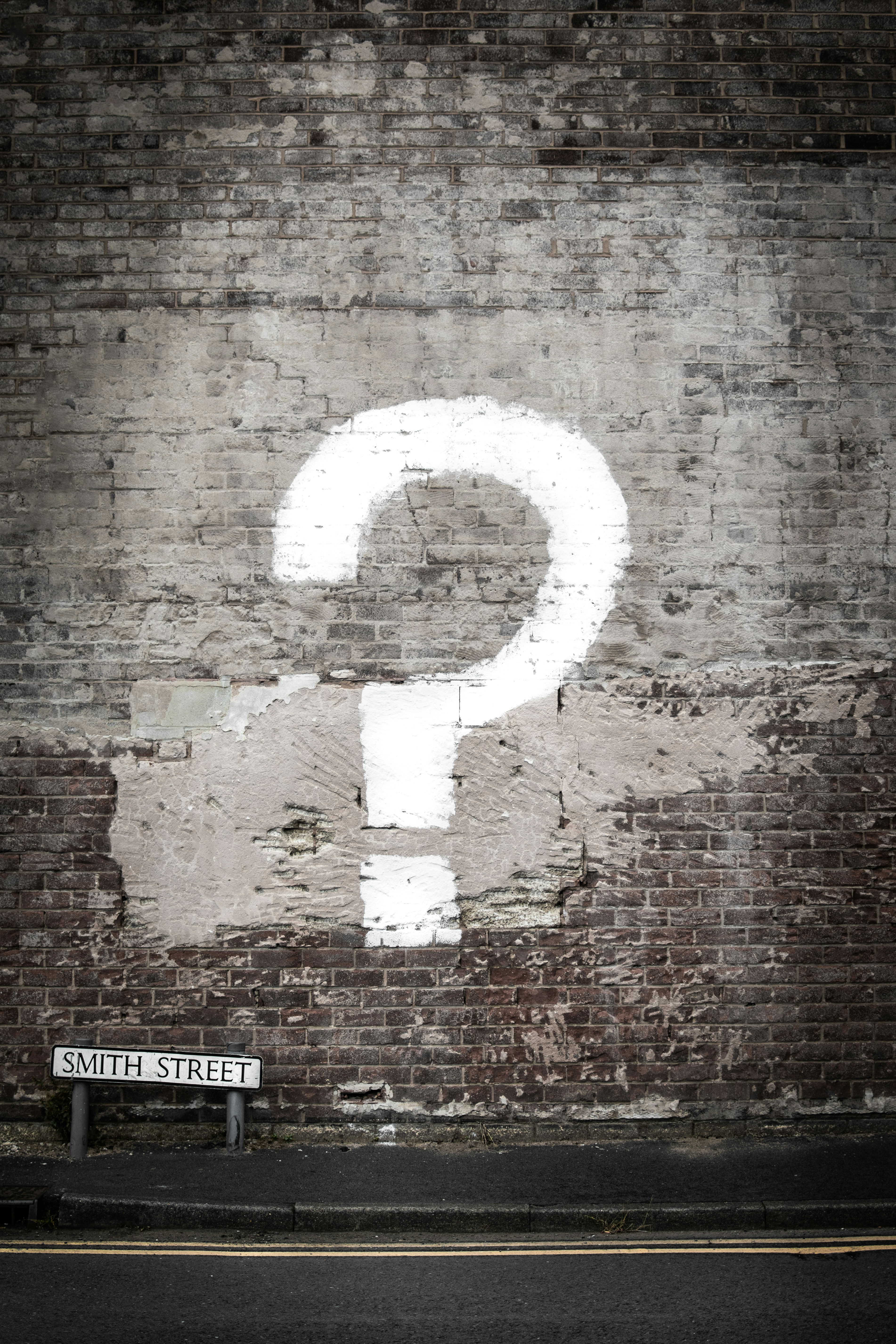 A large white question mark painted on a weathered brick wall above a street sign