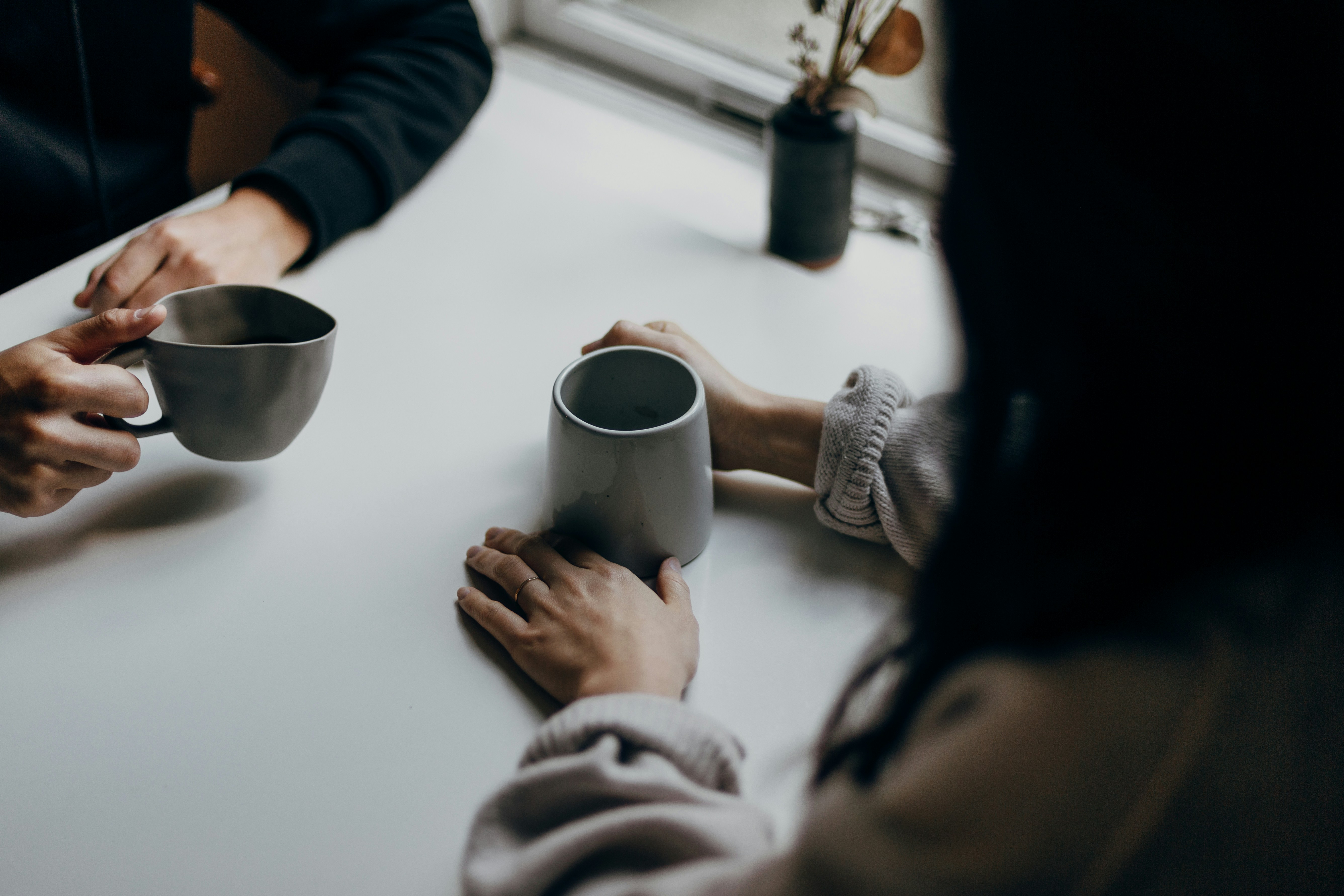 two people holding gray mugs at table