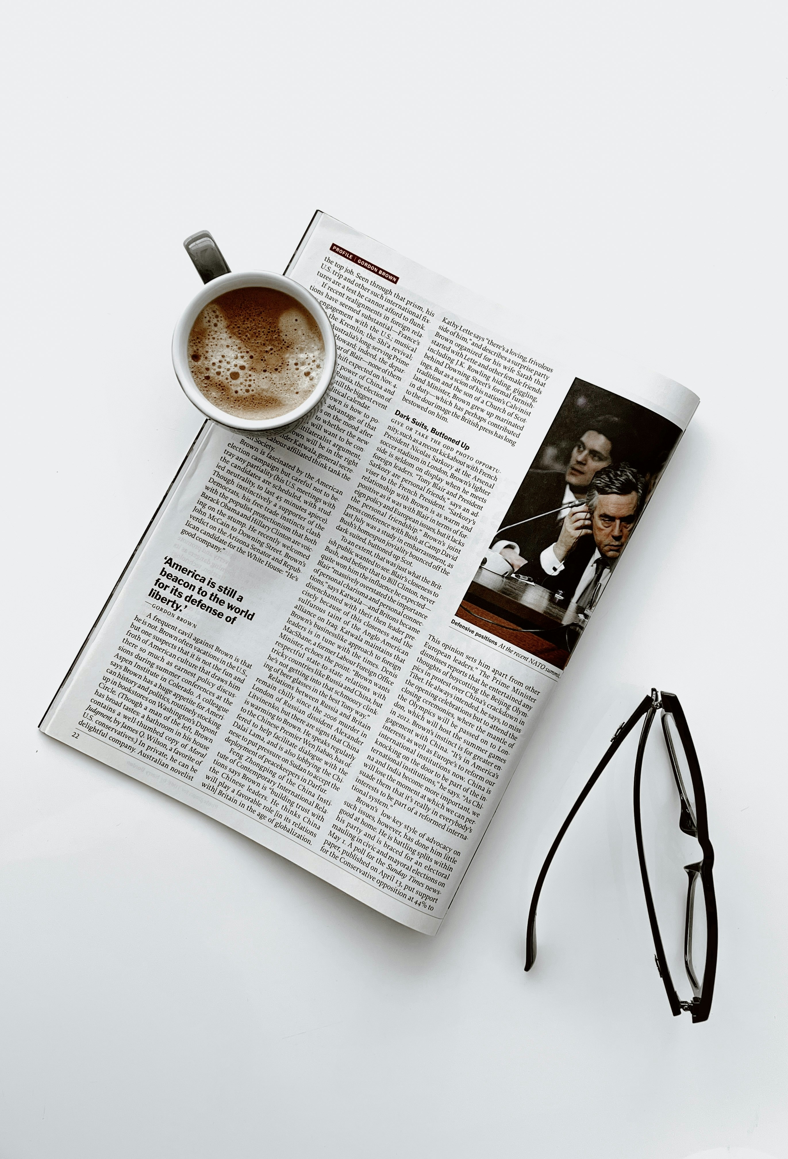 a cup of coffee sitting on top of a newspaper next to a pair of glasses