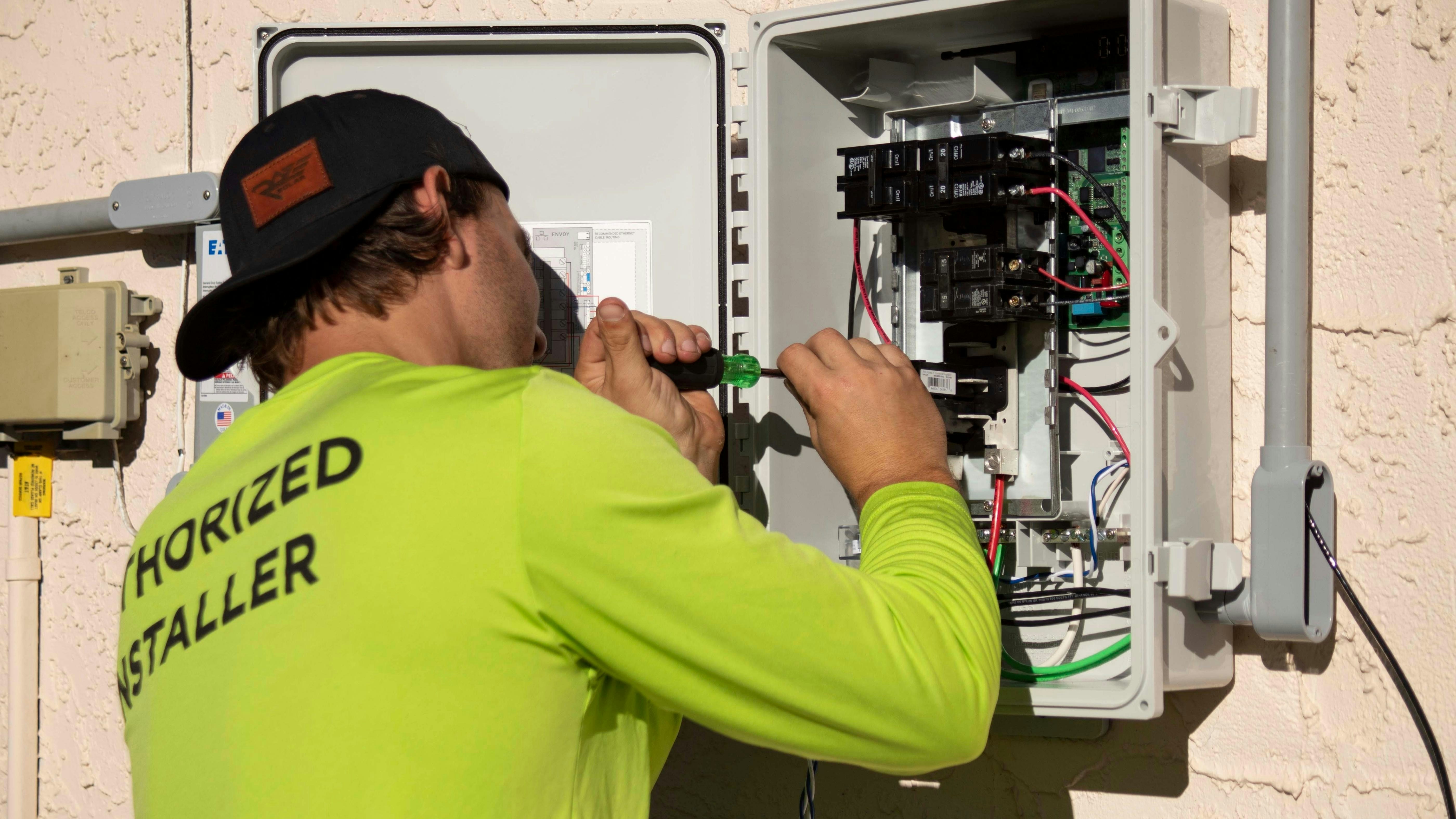 A person in a neon yellow shirt using a screwdriver on an electrical panel