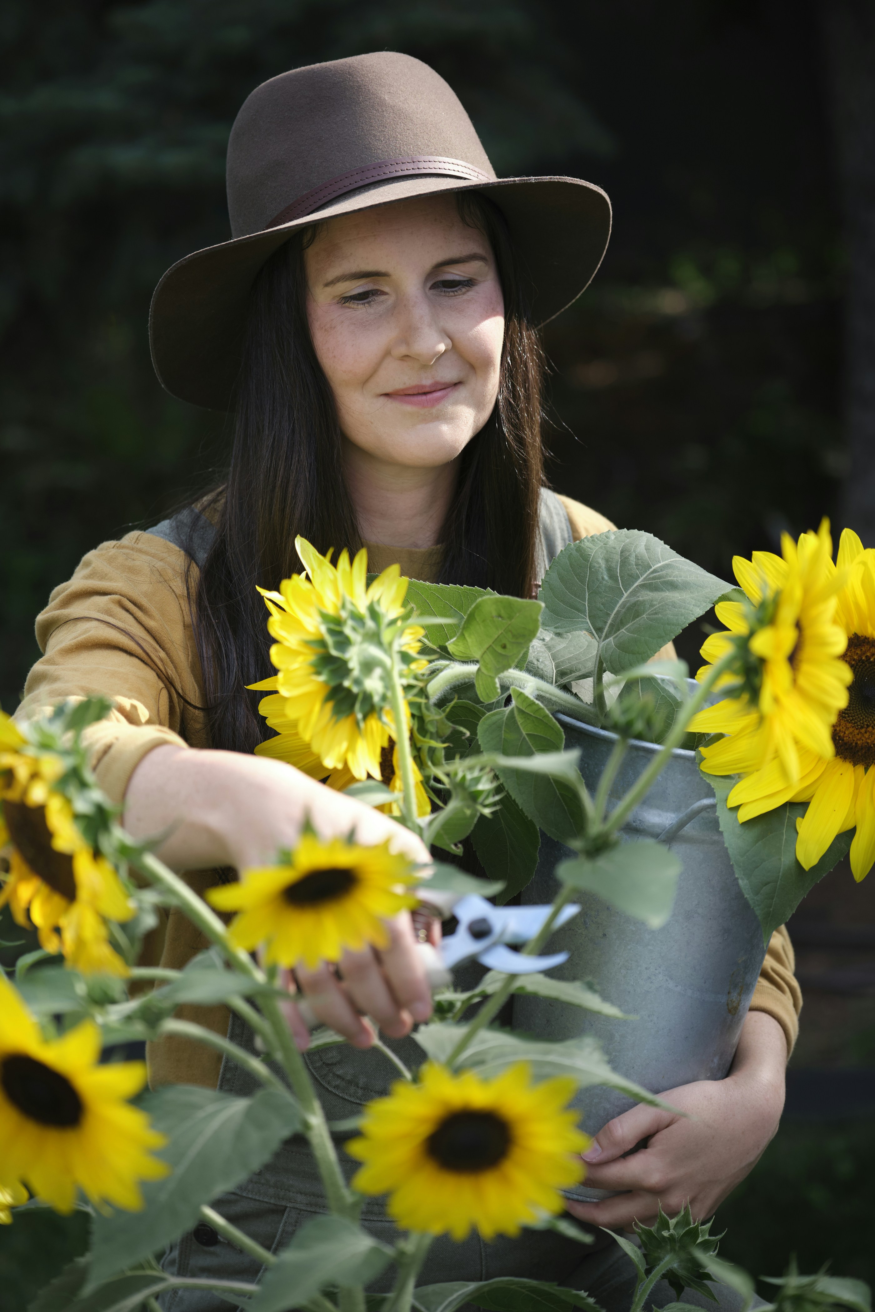 A woman in a hat holding a bucket of sunflowers