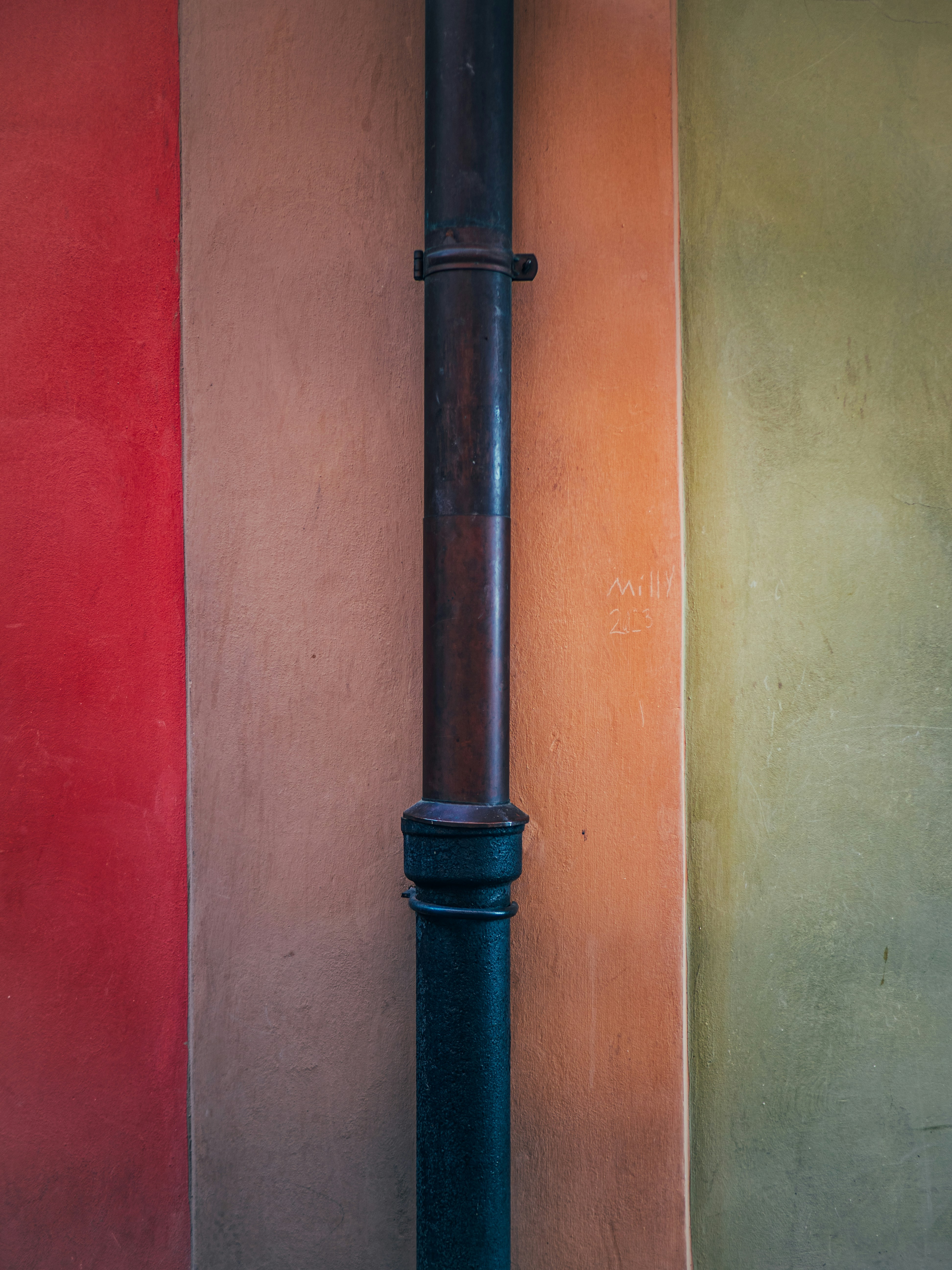 A vertical pipe against a colorful wall.