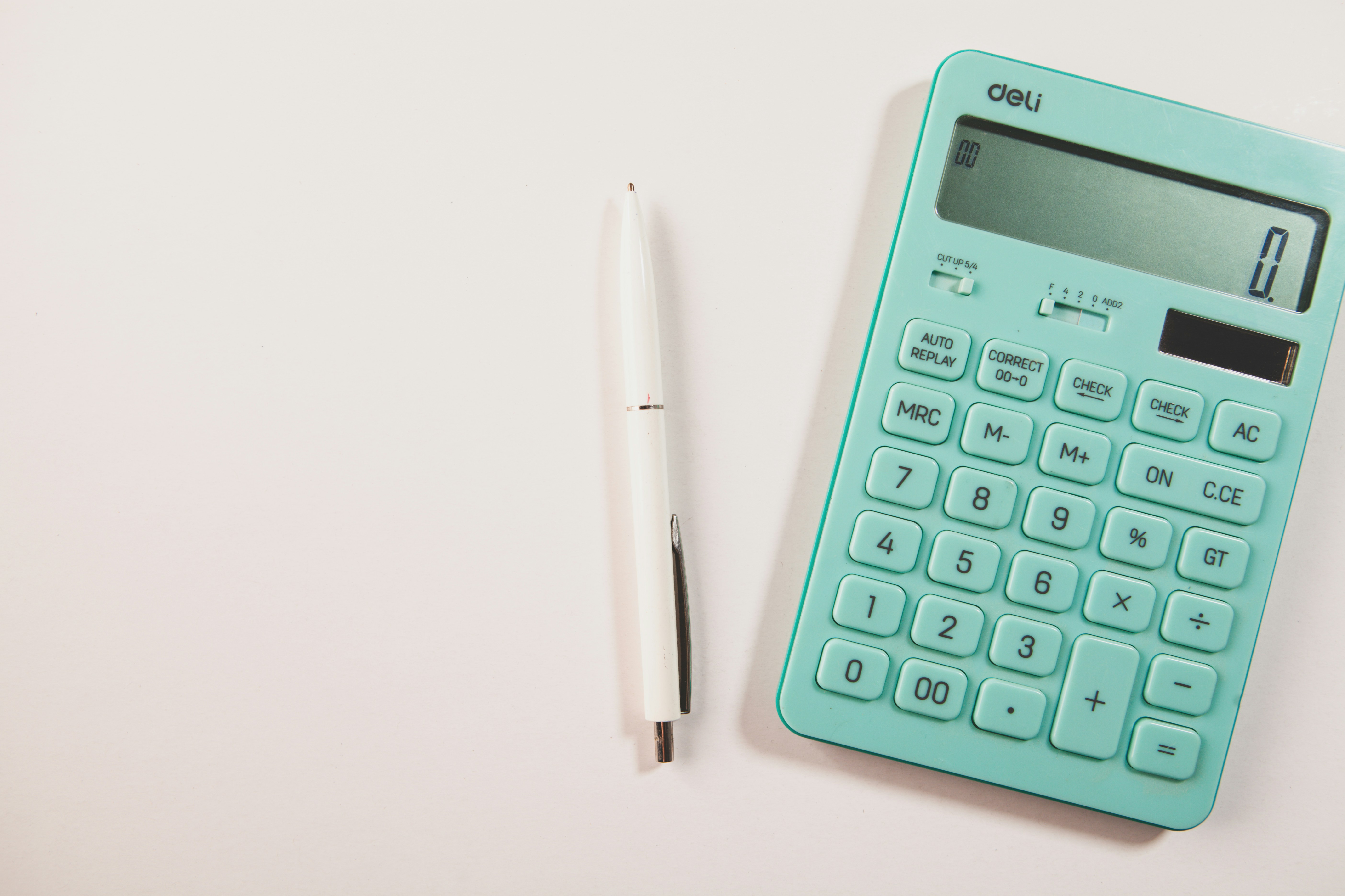A teal calculator and white pen on a white surface.