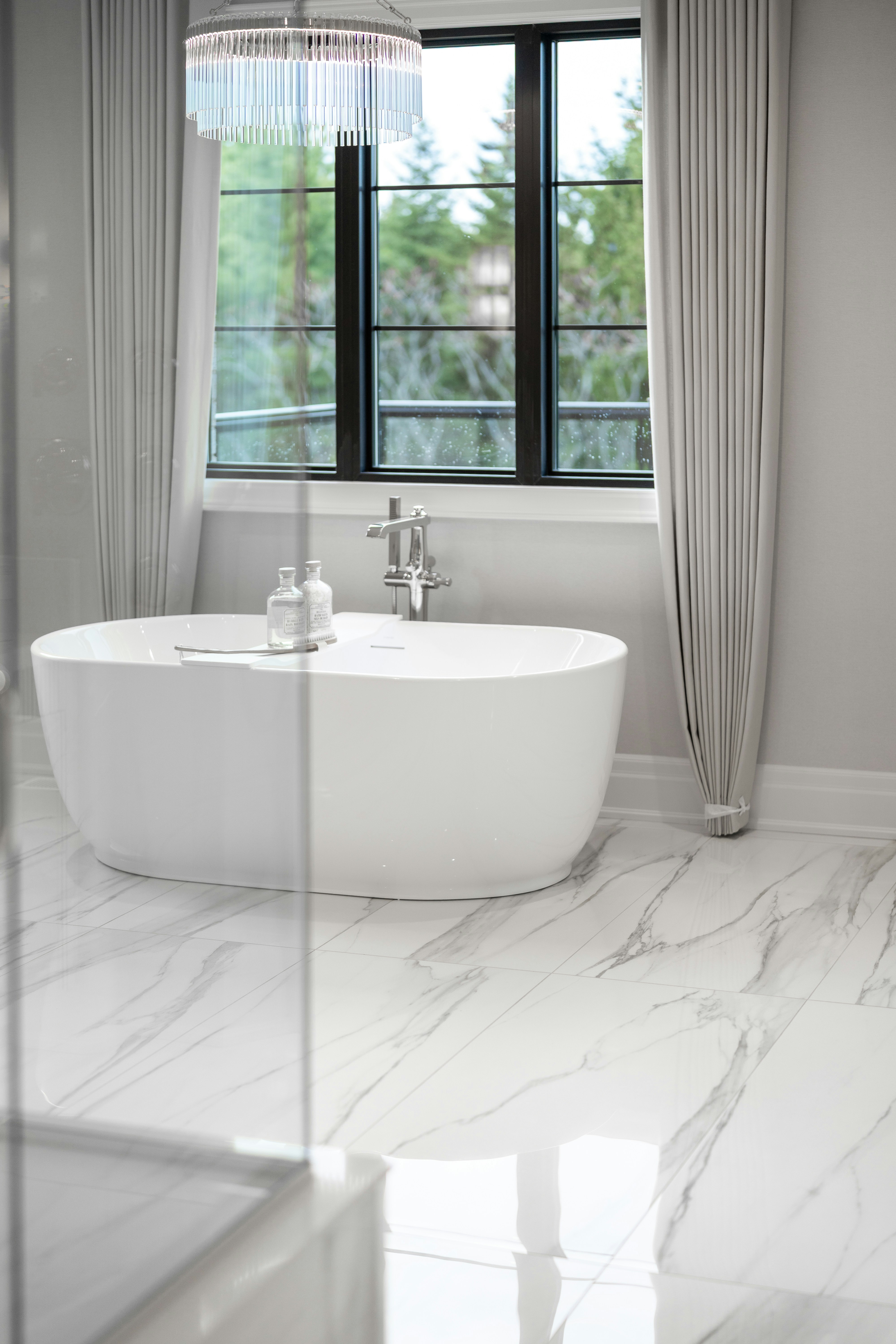 Modern bathroom with a white freestanding bathtub and large window.
