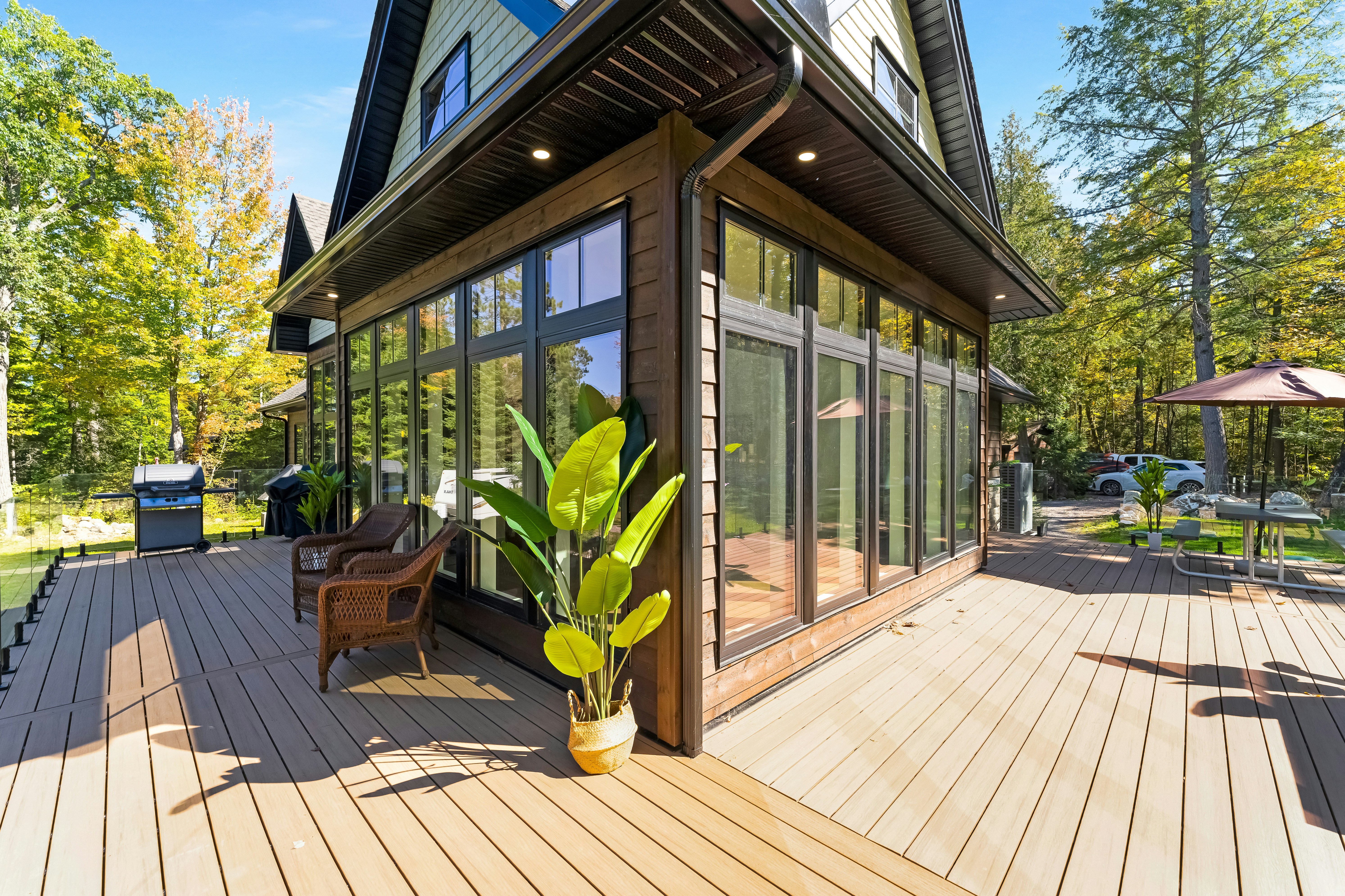 A wooden deck with wicker chairs and a potted plant beside a house